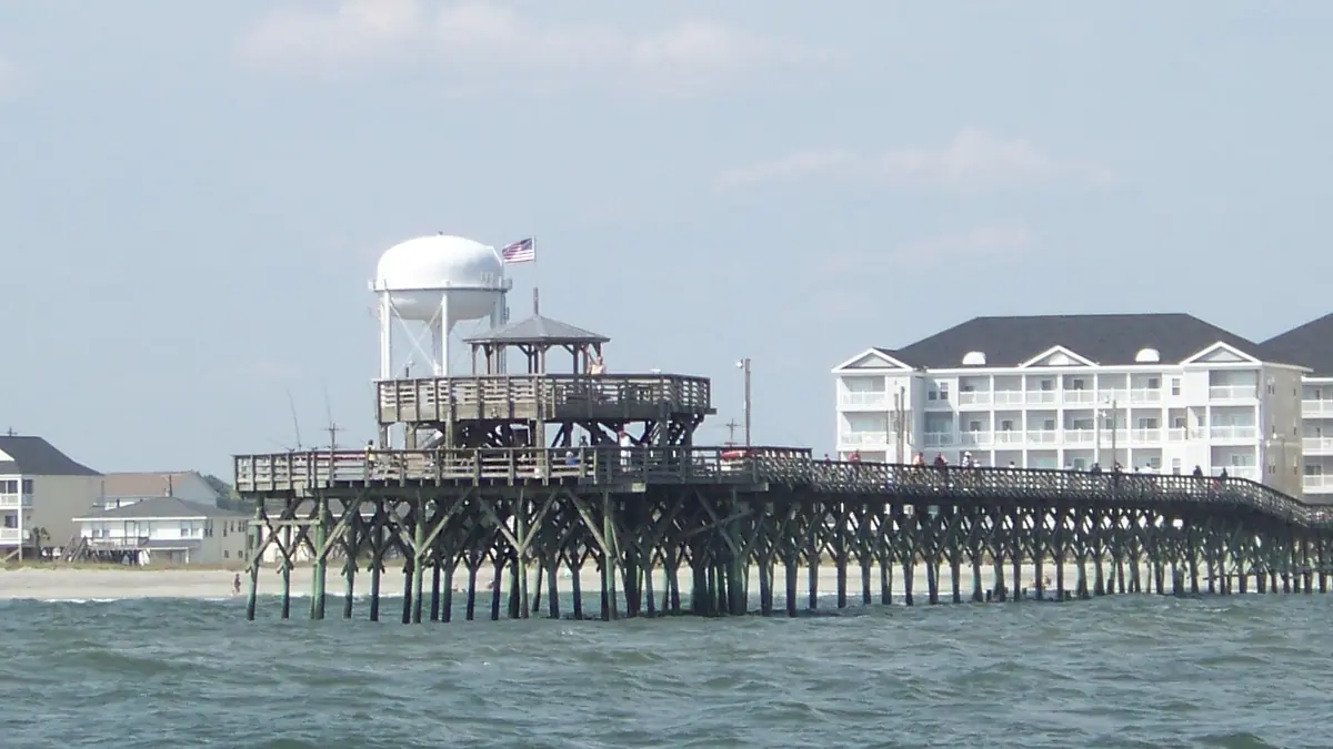 The long wooden Cherry Grove Pier reaching into the ocean in North Myrtle Beach, with beach houses, a water tower and a tall hotel behind it