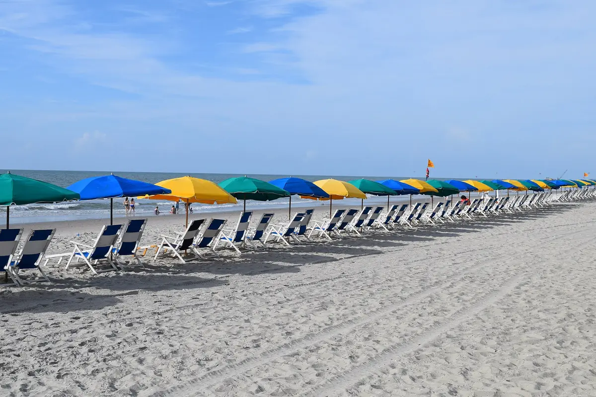 Rows of beach chairs and blue, green and yellow umbrellas on the wide sand beach in North Myrtle Beach