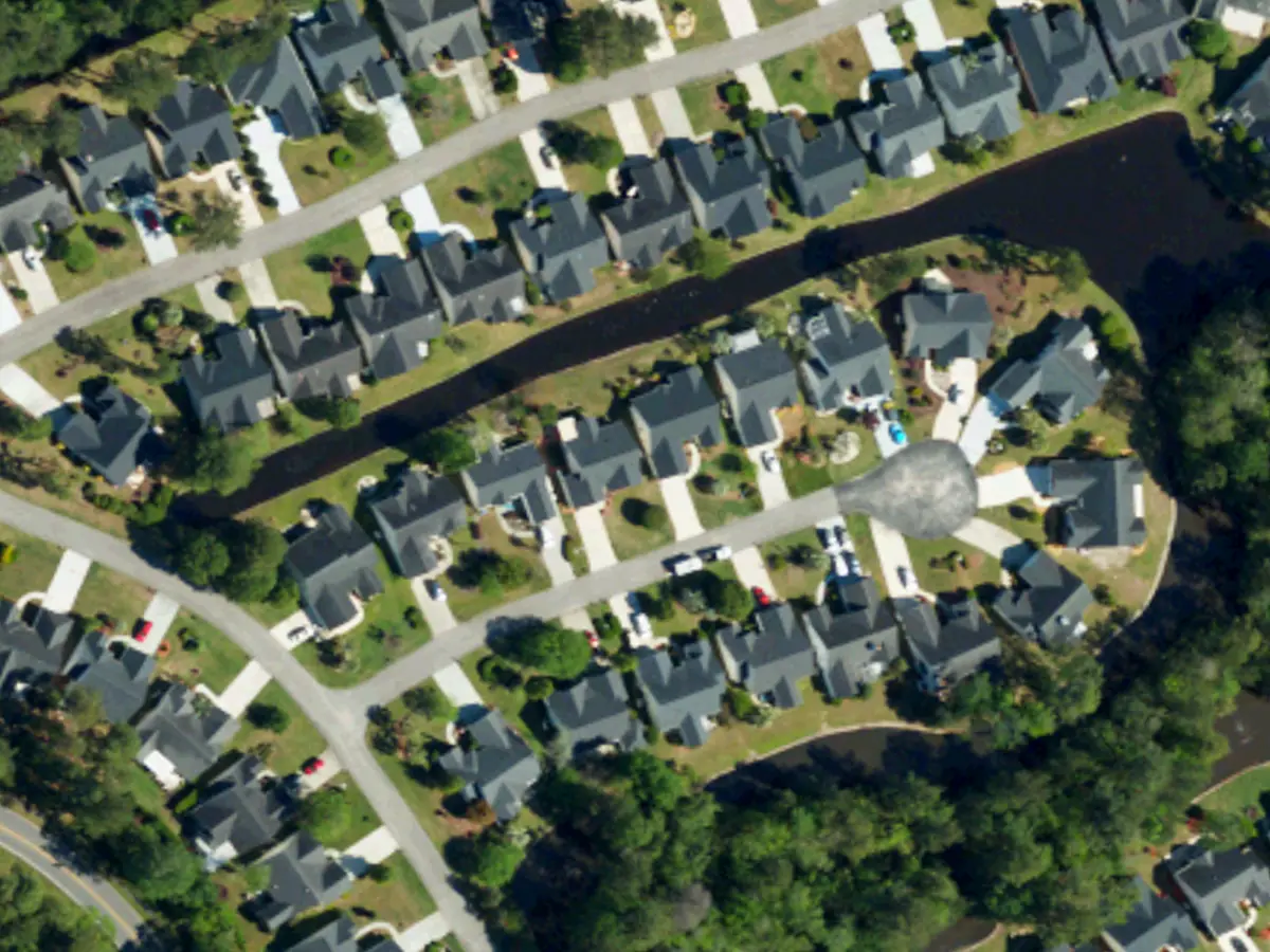 Houses with dark roofs, green yards and trees along two curving streets and a pond in Myrtle Trace, seen from above
