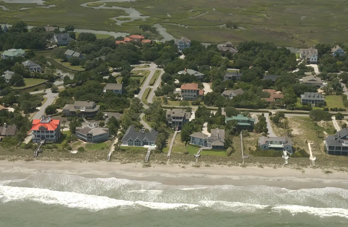 Large beach houses with walkways over the dunes, more houses among dark green oaks behind them, and a wide salt marsh with creeks at the top, at DeBordieu Colony seen from a plane over the ocean