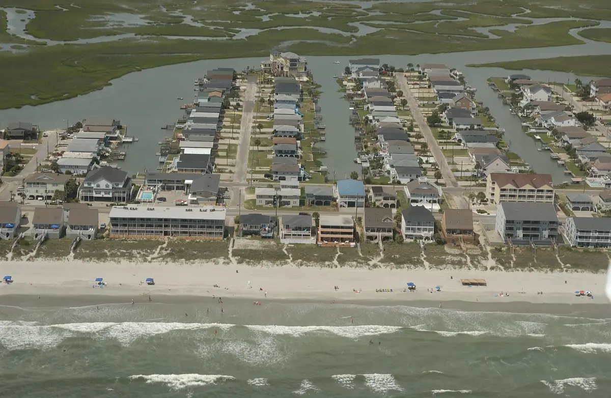 Rows of houses on long canals with boat docks, running back from the beach to a wide green marsh at Cherry Grove, seen from a plane over the ocean