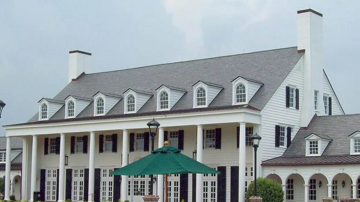 The large white Pine Lakes clubhouse with a row of tall columns, black shutters and dormer windows in a gray roof
